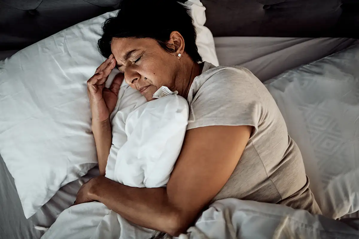 Mujer recostada en cama con la mano en la cabeza, experimentando mareos cervicales.