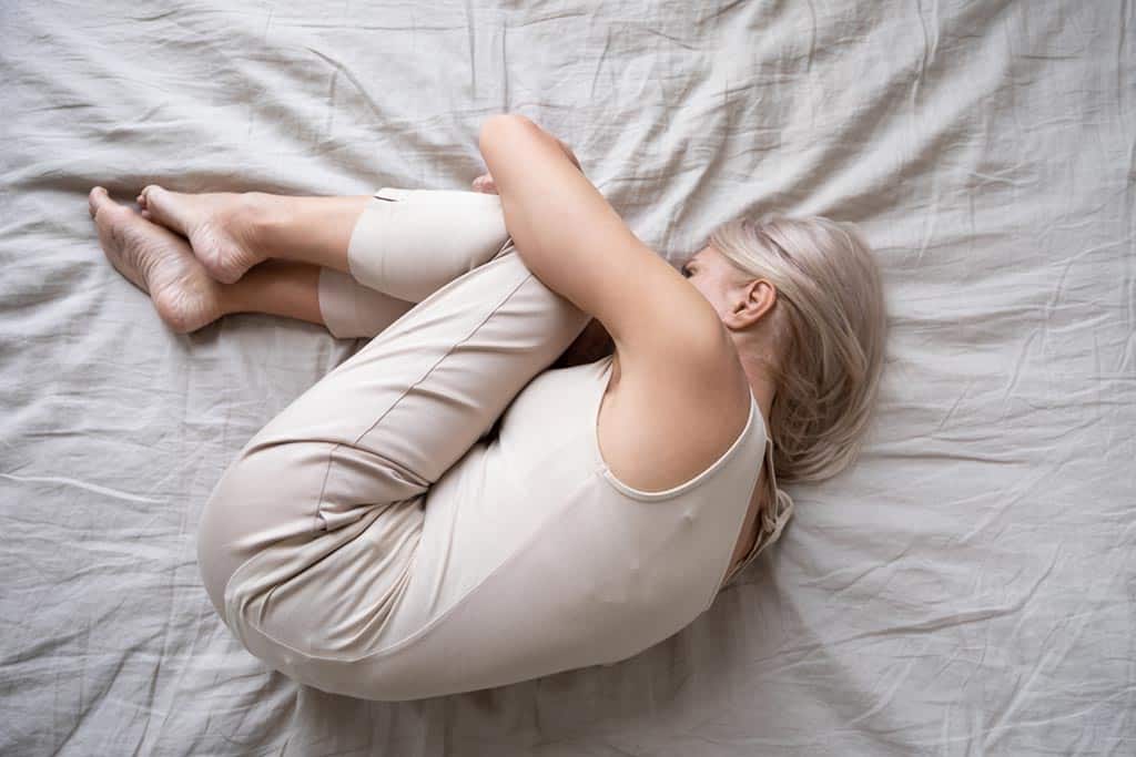 Mujer en posición fetal sobre el colchón de una cama